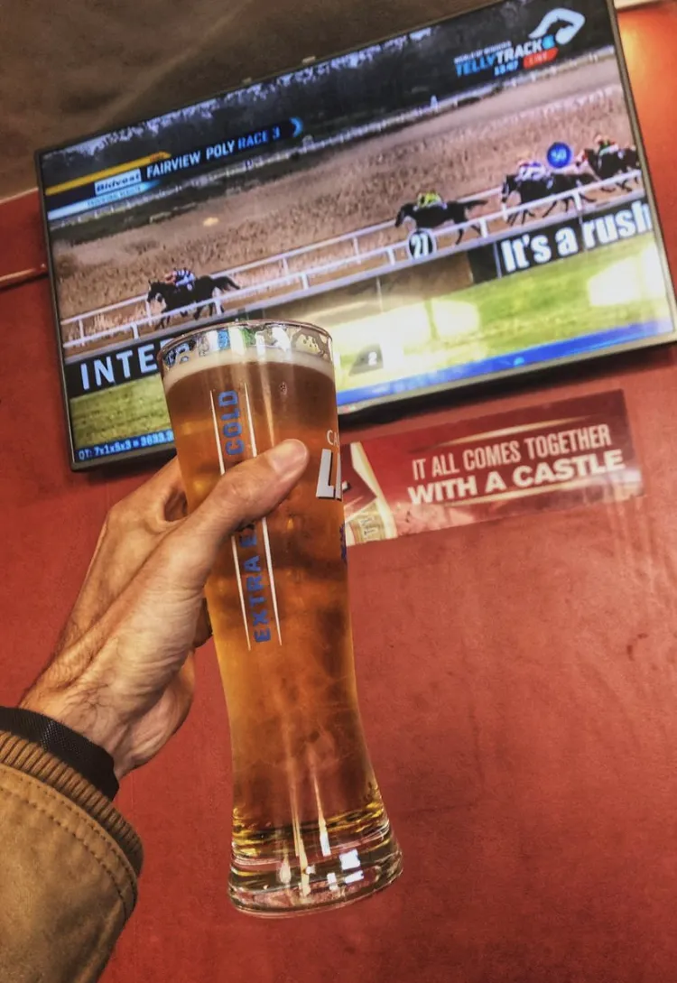 A Castle tank beer held up in front of horse racing on the screen