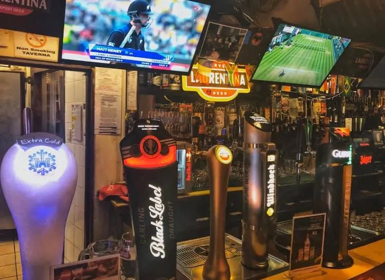 Castle tank beer taps under a row of screens showing live sport